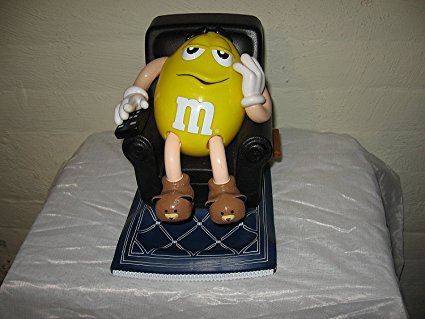 Yellow M & M Candy Dispenser. Sitting in brown Recliner